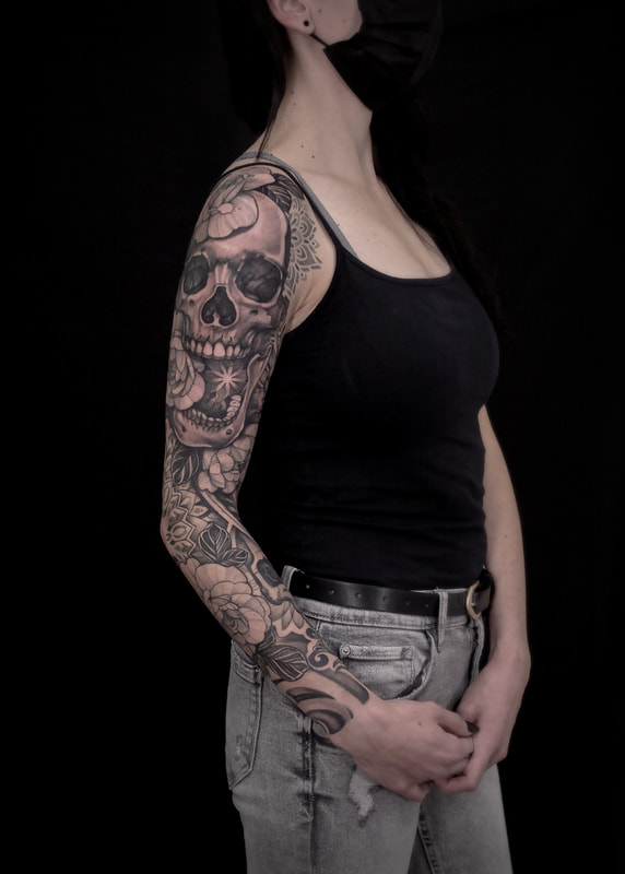 A woman with a full tattoo sleeve of a skull with floral and geometric mandala work